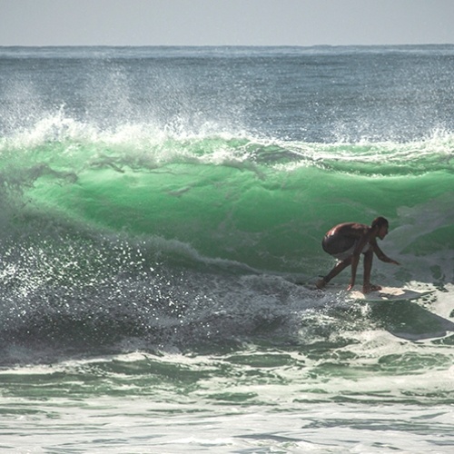 man crouched surfing at Los Cedros